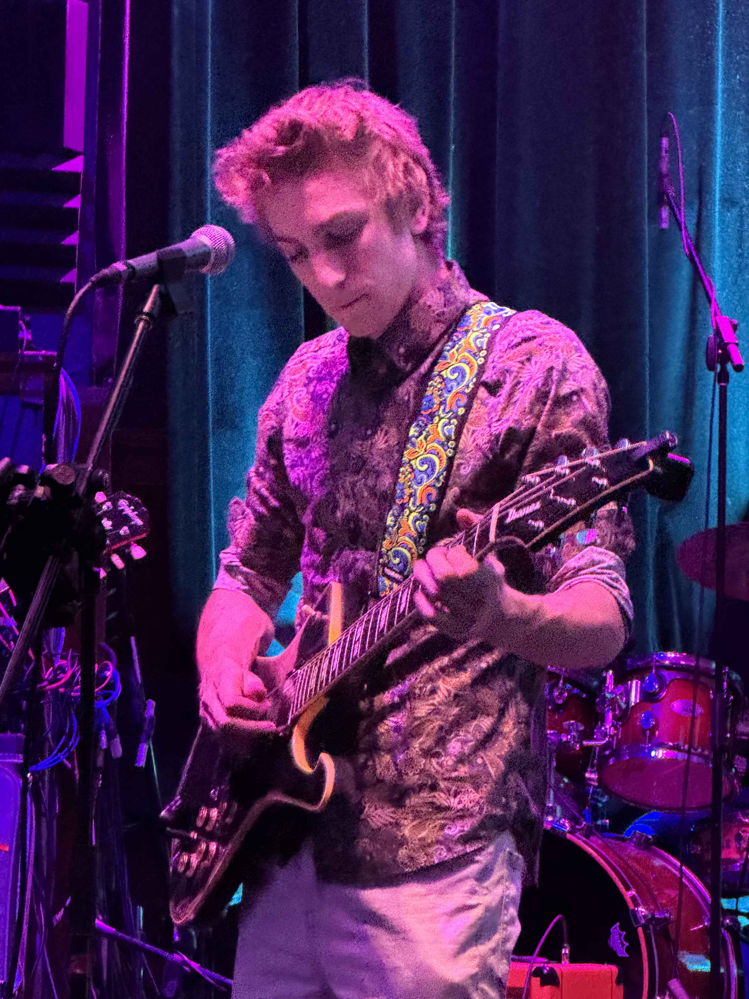 August James performing solo on stage with guitar in purple lighting